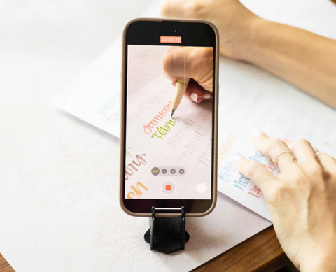 An iPhone on a tripod filming someone drawing