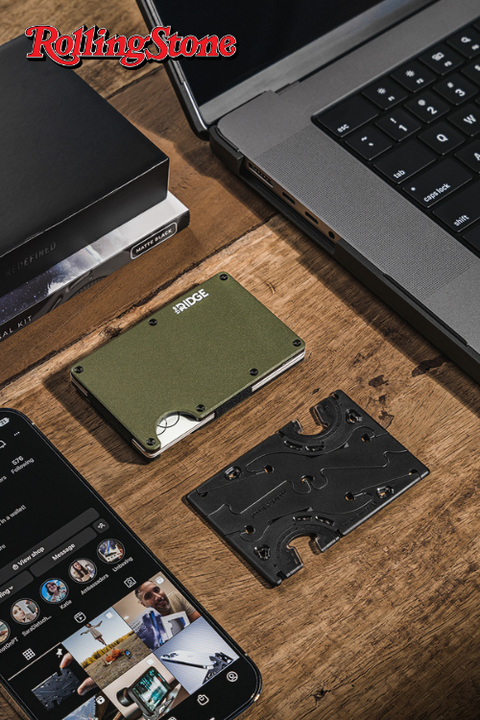 A pocket tripod in card form on a wooden desk with a macbook, a ridge wallet and an iphone and
