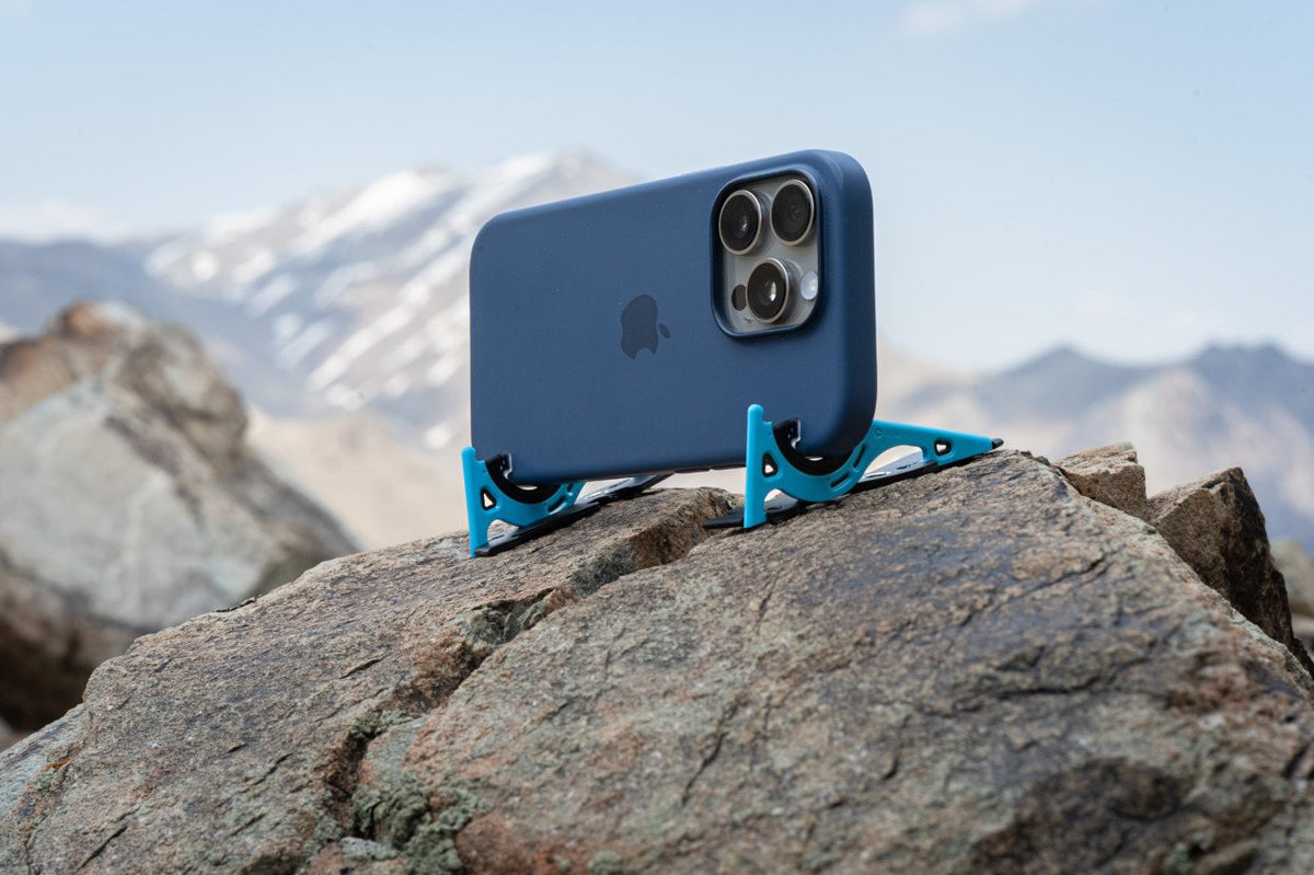 A blue iPhone on a Pocket Tripod on a rock, with snowy mountains behind