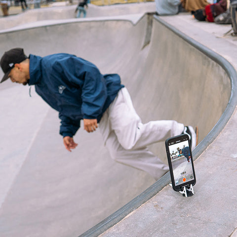 A phone on a Pocket Tripod above ramp capturing a skateboarder at Venice Beach doing a trick below it.
