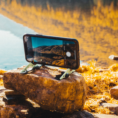 A tripod holding a phone horizontally while taking a picture of a landscape on a rock