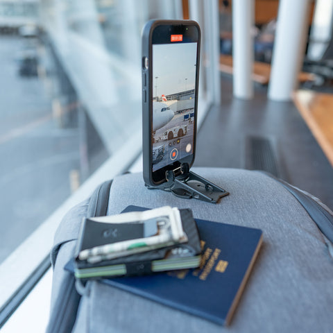 iPhone in tripod stand with wallet and passport on travel bag in airport filming airplane