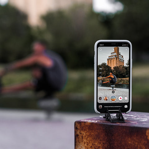 An iphone on a tripod stand taking picture of a man doing a workout in a gym in the background