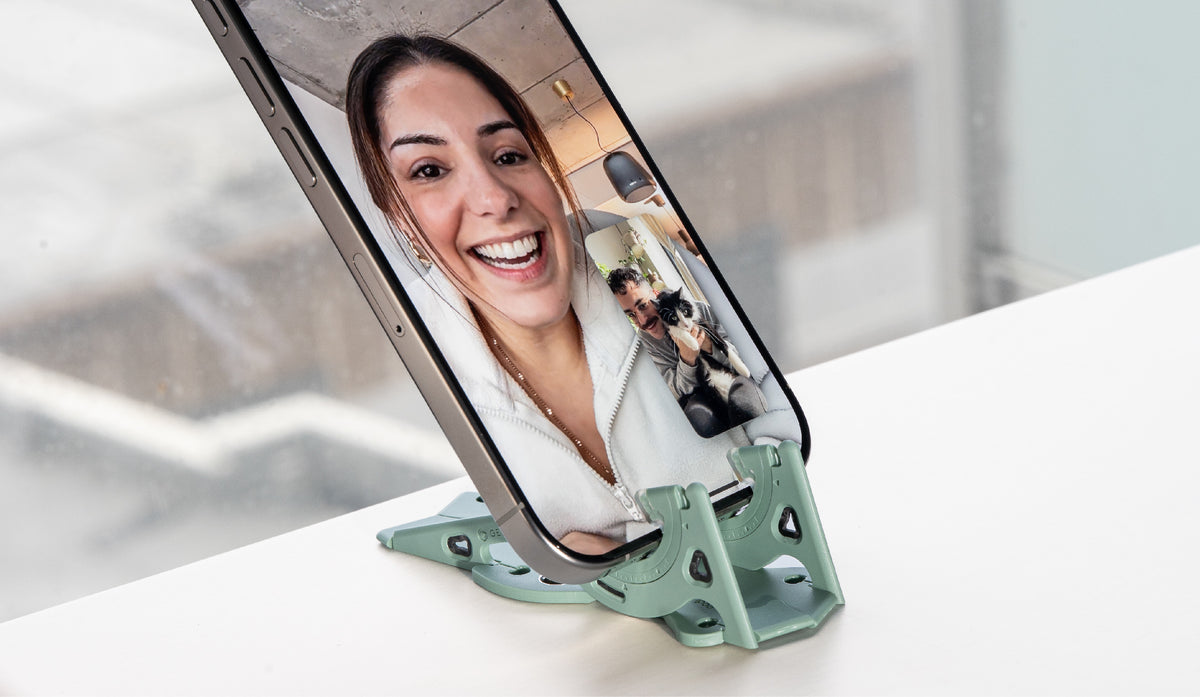 A smiling woman on a video call, on a phone tilted down on a sage green Pocket Tripod