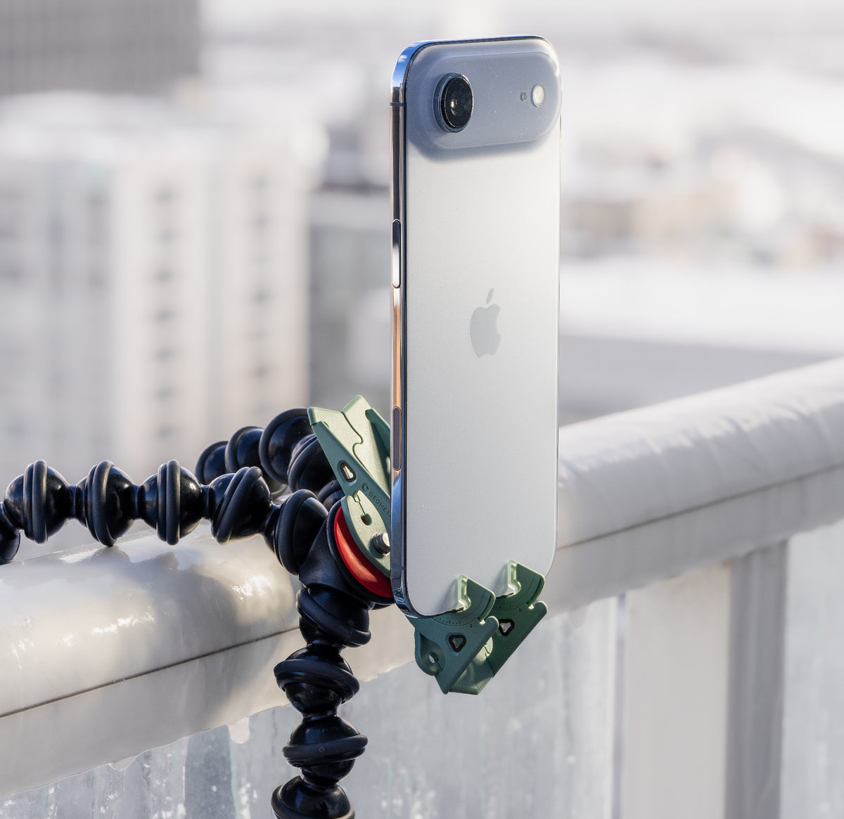 A sage green Pocket Tripod holding a phone on a flexible tripod wrapped around a balcony rail