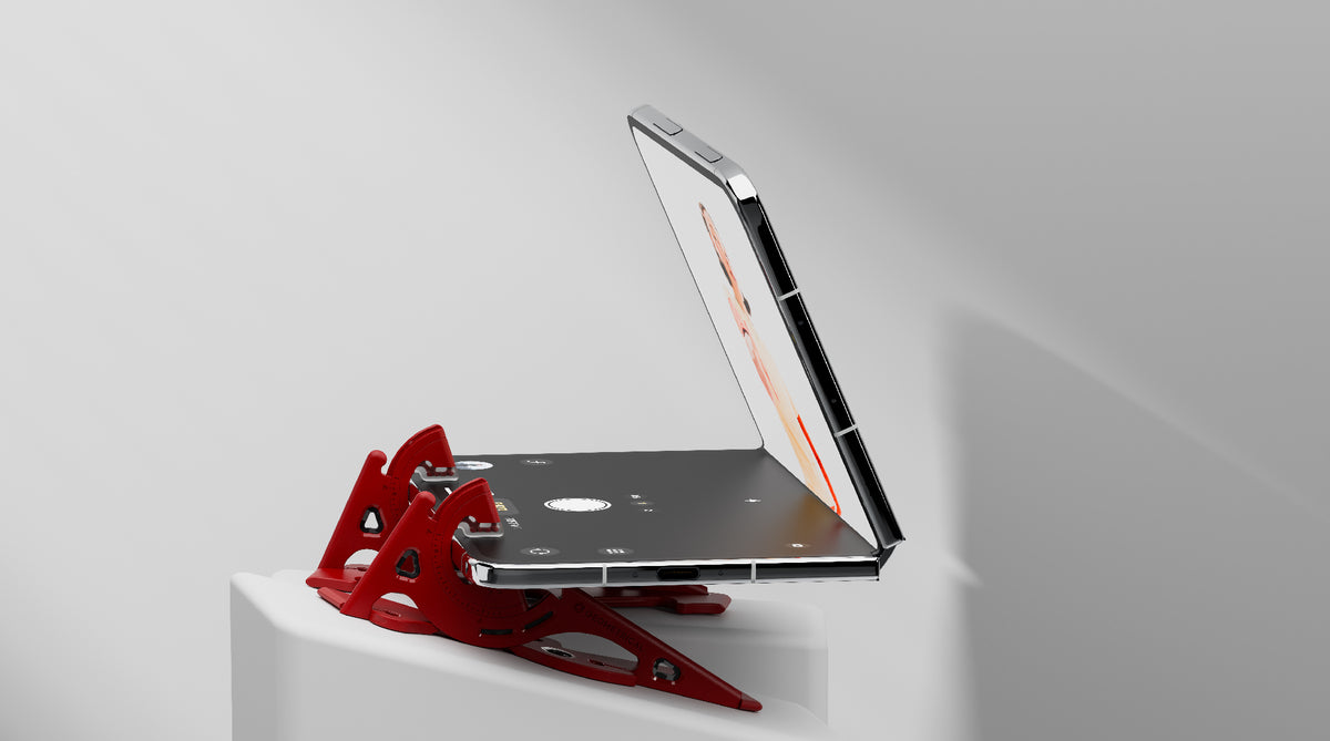 A half-open foldable phone resting on the separated legs of a red Pocket Tripod