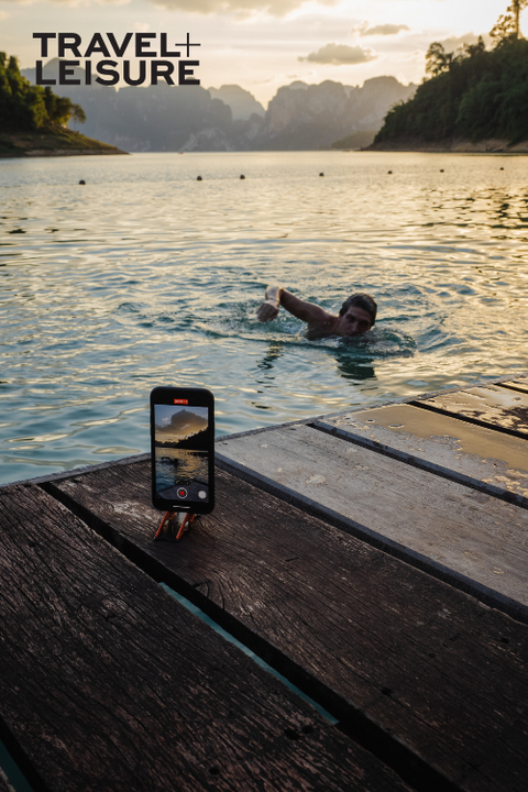an iphone on a pocket tripod on a dock in thailand recording a video of a someone swimming in a river