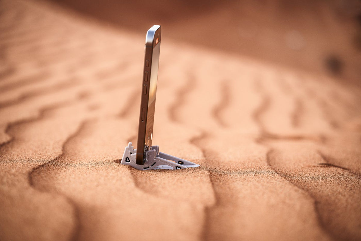A phone standing on a Pocket Tripod in rippled desert sand