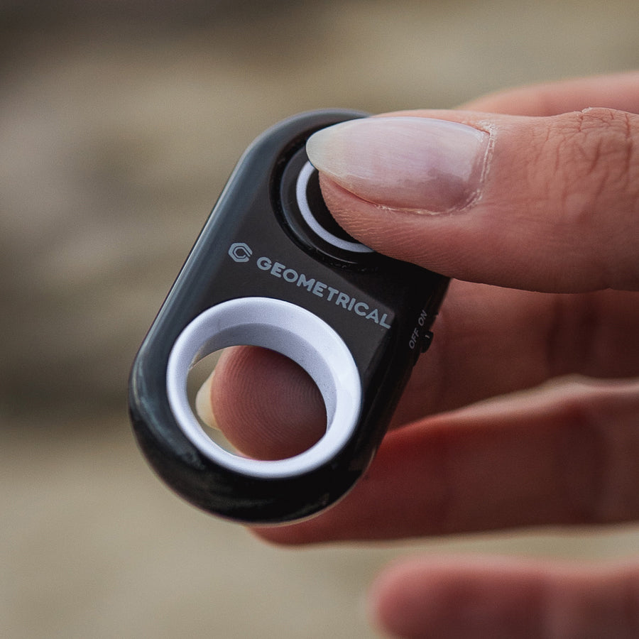 Close-up of a thumb pressing the shutter button on the black Bluetooth remote